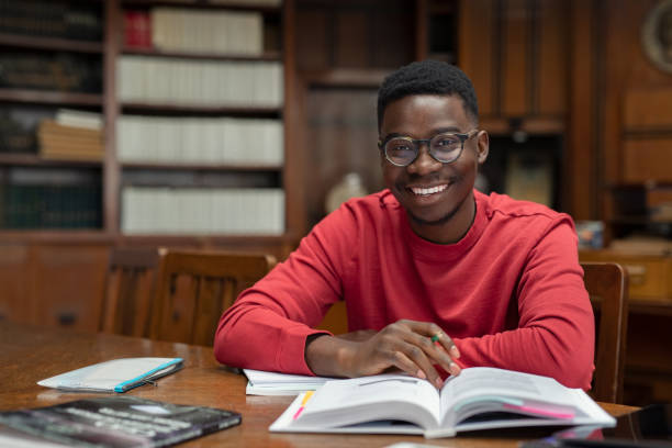 Smiling African student holding books in a library